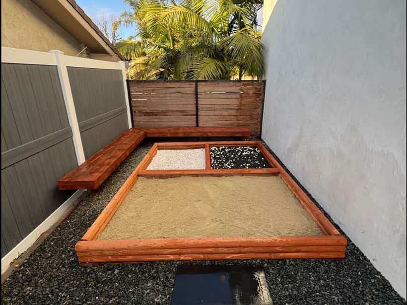 Side yard in black gravel with a redwood sandbox and bench built into it, in the Anaheim area